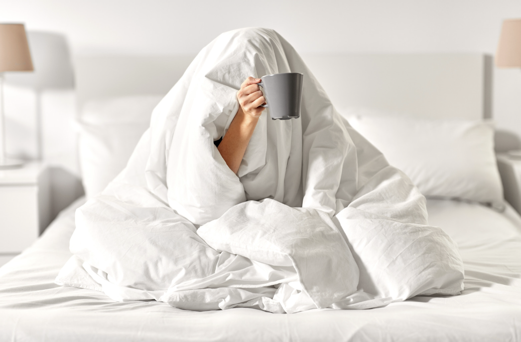 Image shows person wrapped in blanket holding a coffee cup demonstrating the effects of bed rotting that are discussed in this article.